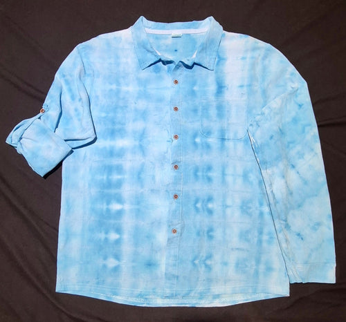 A light blue and white tie-dye long-sleeve button-up shirt laid flat on a dark brown fabric background.