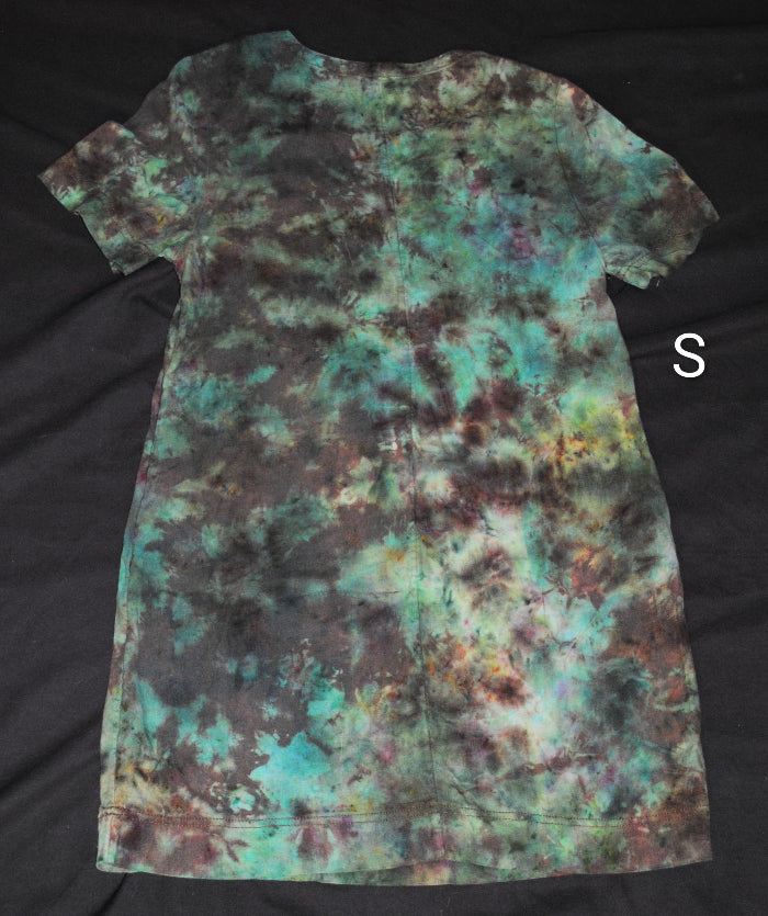 A short-sleeve tie-dye dress laid flat on a black fabric background, featuring a mottled pattern of teal, green, brown, and black. A white letter 'S' is shown to the right of the shirt.