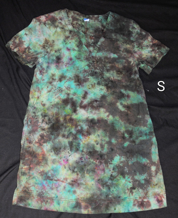 A short-sleeve tie-dye dress laid flat on a black fabric background, featuring a mottled pattern of teal, green, brown, and black. A white letter 'S' is shown to the right of the shirt.
