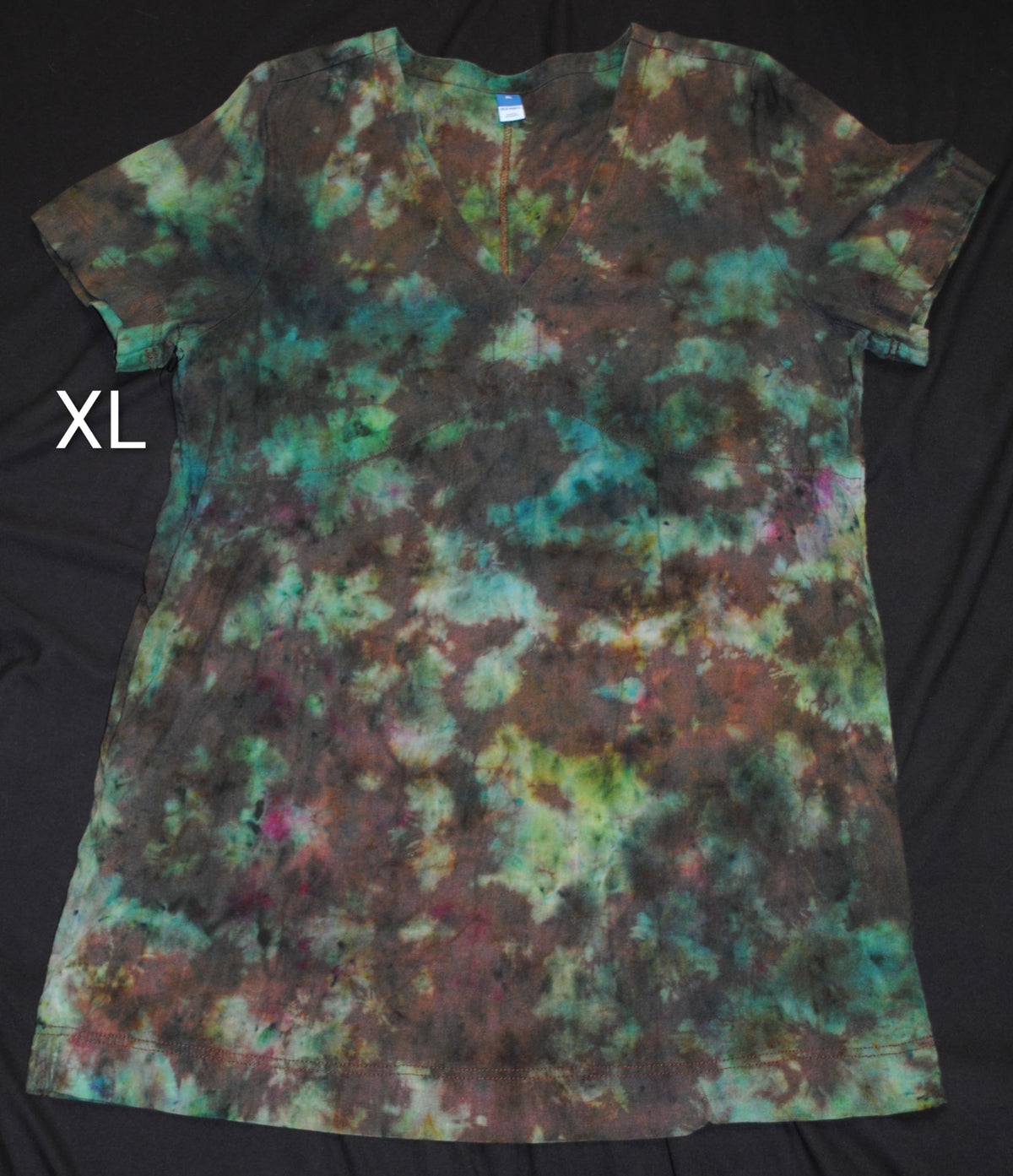 A short-sleeve tie-dye dress laid flat on a black fabric background, featuring a mottled pattern of teal, green, brown, and black. White letters 'XL' is shown to the left of the dress.