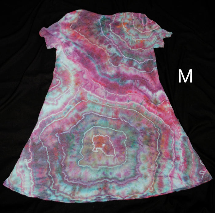 A short-sleeve A-line dress with a vibrant agate slice tie-dye pattern in pink, teal, and white, shown against a solid black background with a size label 'M' on the right.