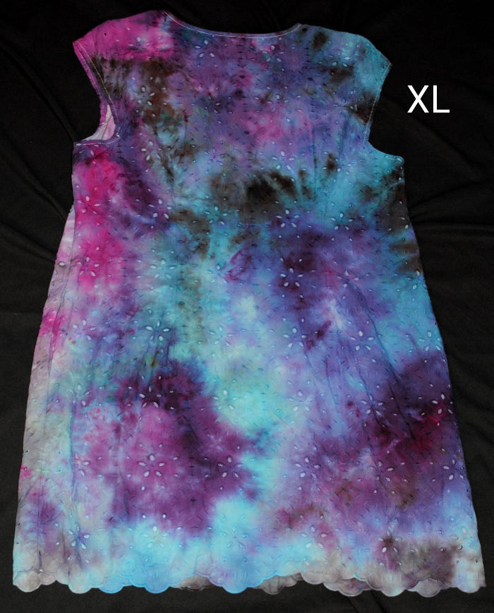 A sleeveless A-line dress with a vibrant tie-dye galaxy pattern in purple, blue, and pink, laid flat on a black background with an 'XL' size label in the top right corner.