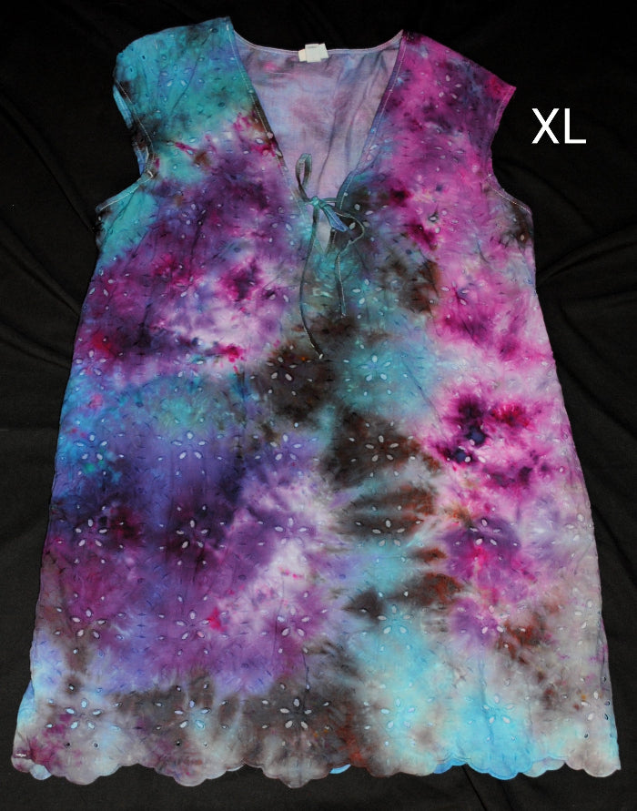 A sleeveless V-neck tie-dye top with eyelet embroidery, shown flat on a black background. The garment features a vibrant spiral tie-dye pattern in purple, pink, blue, and brown, with a scalloped hem.